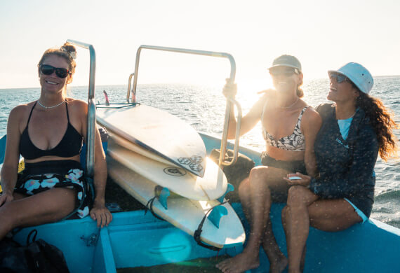 Three travelers on a boat with surfboards during a customised adventure trip