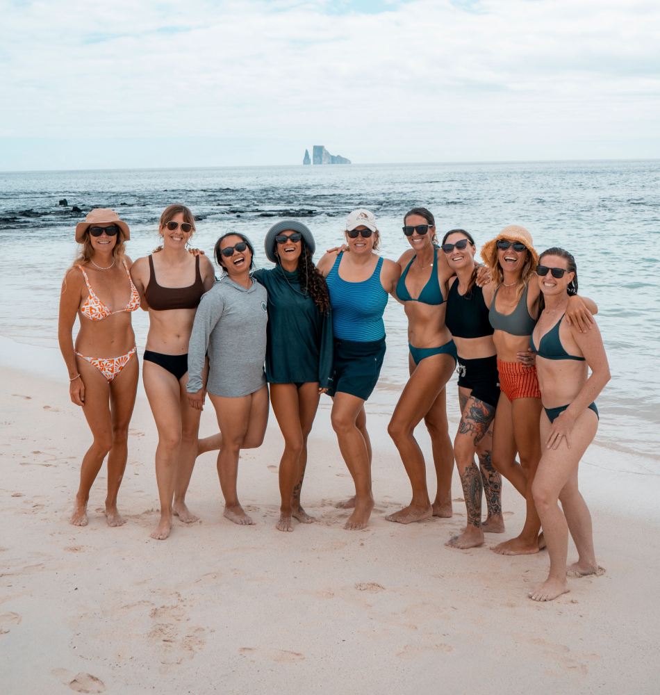 Group of travelers on the beach with Kicker Rock in the background during the Surf and Nature Connection Retreat